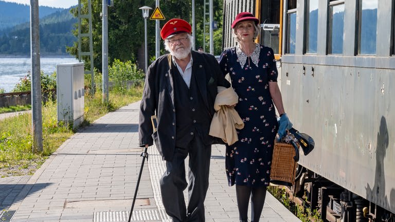 Hermann und Irene gehen am Bahnsteig neben einem alten Postwaggon her