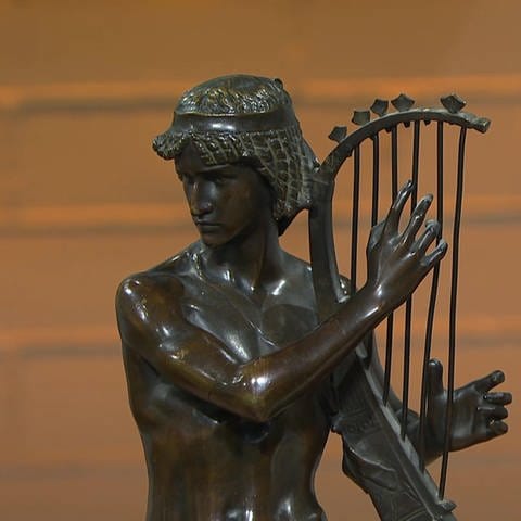 Die Bronzefigur eines Mannes der auf der Hafe spielt