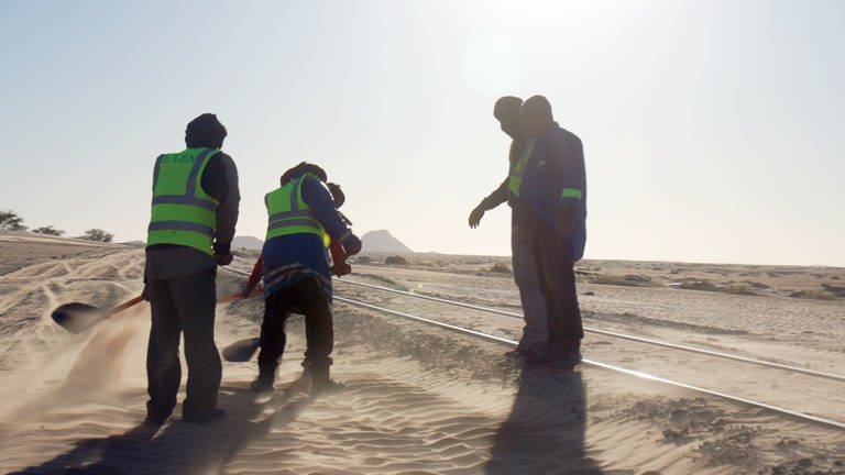 Ein Sandräum-Team schippt Sand von den Schienen, damit der Zug nicht entgleist.  
