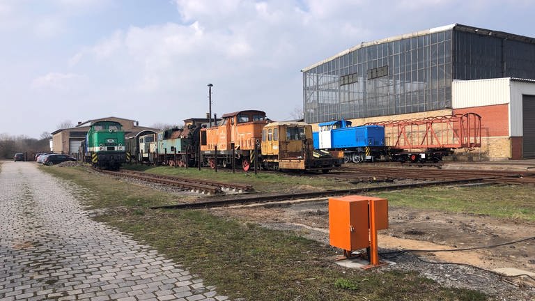 Vor der Halle warten etliche historische Schienenfahrzeuge auf Reparatur und Wiederinbetriebsetzung. 