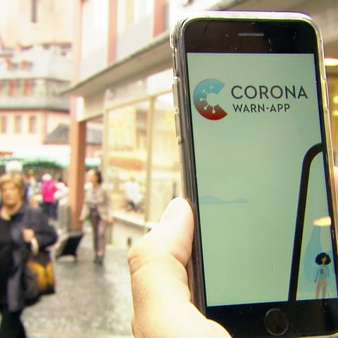 Handy mit Corona Warn-App auf dem Bildschirm wird rechts ins Bild gehalten