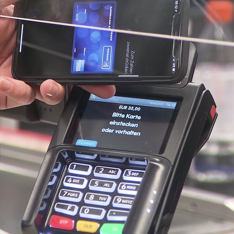 Anonyme Hand hält Smartphone an Kartenlesegerät an Supermarktkasse