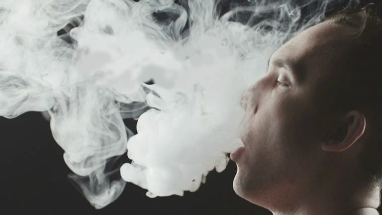 Konsumentvon E-Zigaretten stößt Dampfwolke aus. Ansicht im Profil.