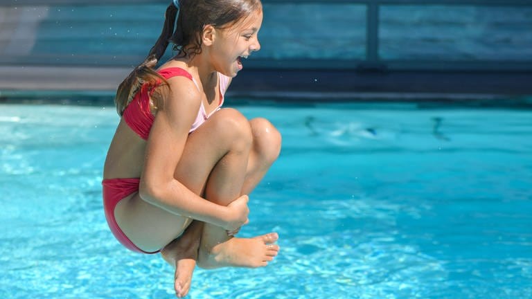 Bei sommerlich warmen 34 Grad Celsius springt ein Mädchen in einen Gartenpool. 