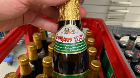 Hand hebt Tannenzäpfle-Bierflasche mit goldener Manschette aus Bierkasten.