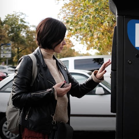 Frau steht vor einem Parkscheinautomat. Probleme mit KI-Parkkontrollen - Autofahrer sollen zahlen