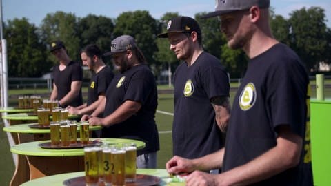 Junge Männer der Football-Mannschaft "Bulldogs" stehen vor Stehtischen mit vollen Biergläsern. Qualität, Geschmack, Nachhaltigkeit von Rothaus Tannenzäpfle