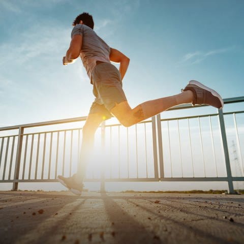 Mann joggt in Sportkleidung auf einer Brücke bei Sonnenschein. Warum ihr jetzt mit Sport anfangen solltet