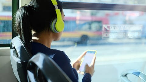 Ein Mädchen sitzt im Bus und hört Musik über Kopfhörer. 
