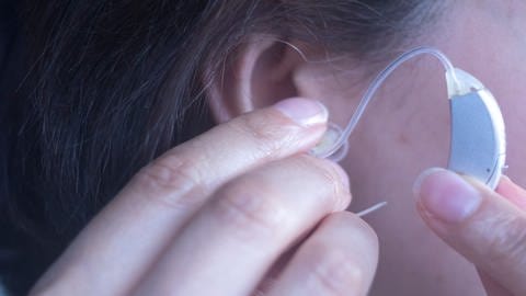 Eine Frau steckt sich ein Hörgerät ins Ohr