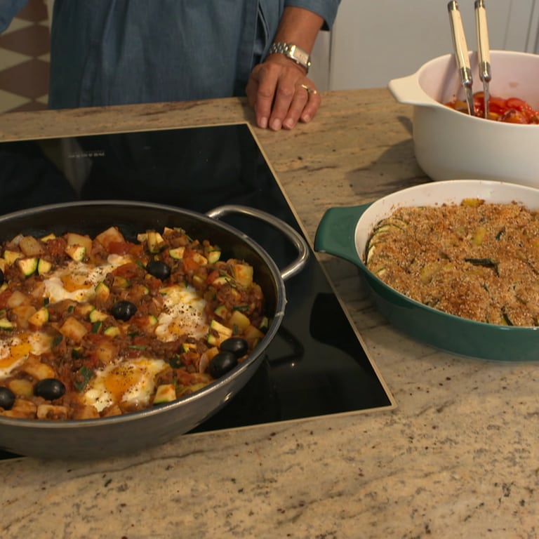 Zucchini-Auflauf und Shakshuka in einer Auflaufform bzw. einer Pfanne auf dem Kochfeld einer Küche. Rezepte bei Marktcheck.