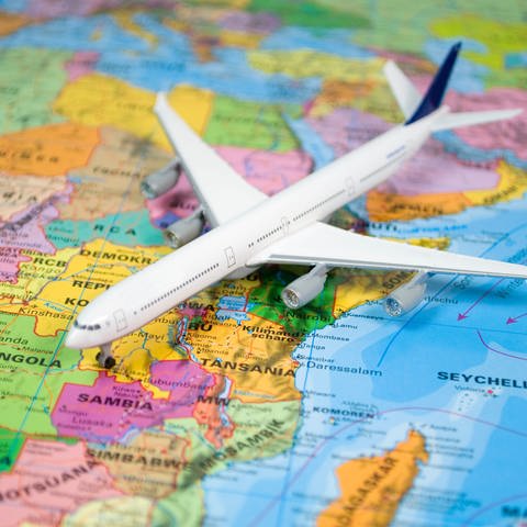 Ein Spielzeugflieger liegt auf einer Landkarte. Was können Fluggäste tun, wenn der Flug abgesagt wird? Welche Rechte haben Fluggäste? 