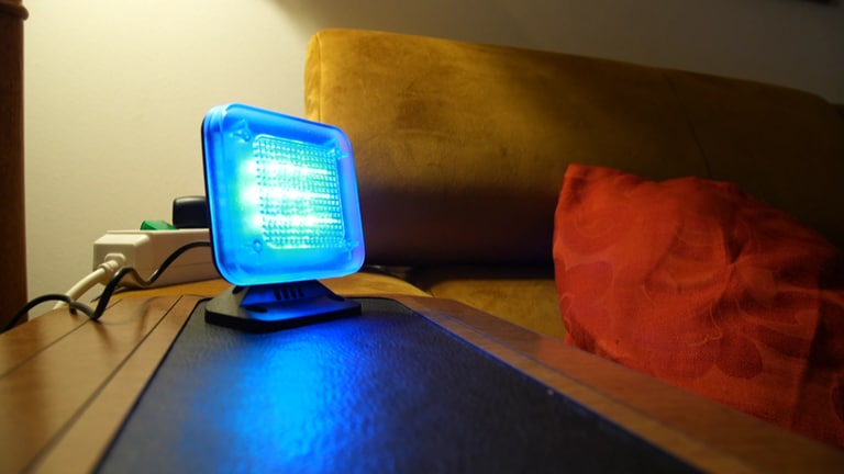 Ein Fernsehsimulator ist ein Gerät, das die typischen bläulich-flackernden Reflexionen eines laufenden Fernsehers abstrahlt. Dadurch soll der Eindruck erweckt werden, dass jemand zu Hause ist. TV-Simulator steht im Wohnzimmer und leuchtet blau.