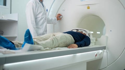 Ein Arzt in weißem Kittel fährt einen Patienten auf einer Liege in die runde MRT Röhre.