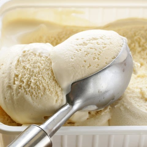 Eine Kugel Vanilleeis wird aus einer Eis-Box genommen. Vanilleeis im Test - welches Eis aus dem Supermarkt schmeckt wie von der Eisdiele?