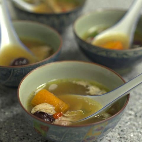 Vier asiatische Suppenschüsselchen gefüllt mit klarer Brühe