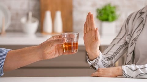 Die linke Person hält der anderen Person ein Glas mit Alkohol hin. Die rechte Person hält ihre Hand als "Stopp-Zeichen". Sie verweigert somit den Alkohol.