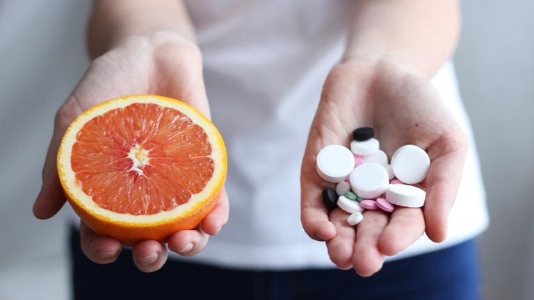 Die Einnahme von Medikamenten in Kombination mit Nahrungsmitteln kann zu Wechselwirkungen führen. Worauf Sie bei der Einnahme von Arzneimittel achten sollten. Eine Frau hält in einer Hand eine Grapefruit und in der anderen Hand Tabletten.