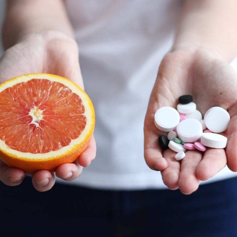 Die Einnahme von Medikamenten in Kombination mit Nahrungsmitteln kann zu Wechselwirkungen führen. Worauf Sie bei der Einnahme von Arzneimittel achten sollten. Eine Frau hält in einer Hand eine Grapefruit und in der anderen Hand Tabletten.