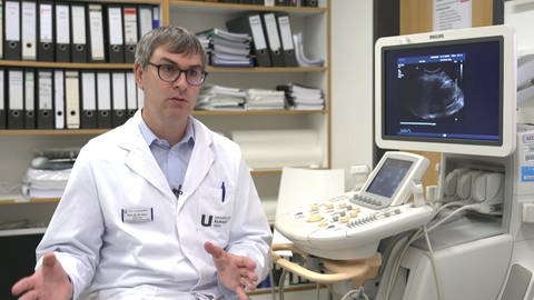 Prof. Martin Heni, Endokrinologe an der Uniklinik Ulm, sitzt vor einem Regal mit Akten und neben einem Ultraschall-Gerät