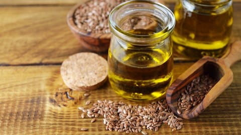 Öl in Gläschen steht neben Leinsamen. Leinöl ist besonders reich an Omega-3-Fettsäuren und damit sehr gesund.