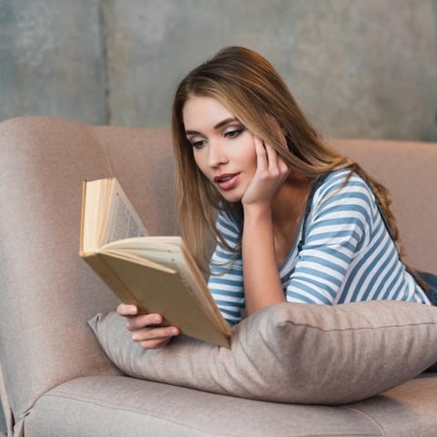 Frau liegt auf einem Sofa und liest ein Buch