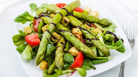 Ein gemischter Salat mit mehreren grünen Spargelstangen, über die Balsamicocreme geträufelt ist