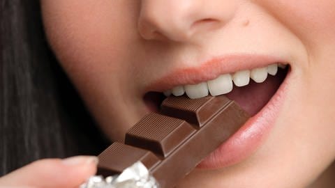 Junge Frau beisst genussvoll von einer Schokolade ab