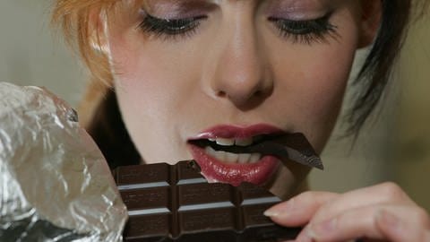 Junge Frau bisst genussvoll von einer Tafel Schokolade ab