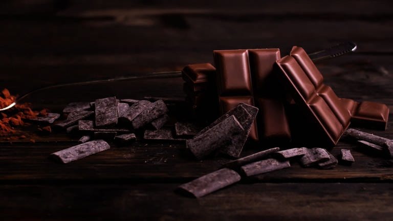 Mehrere Tafeln dunkle Schokolade liegen auf dunklem Holz. Superfood: Schokolade mit einem hohen Kakaoanteil enthält viele gesunde Inhaltsstoffe. Einige können gesundheitlich sogar etwas bewirken.