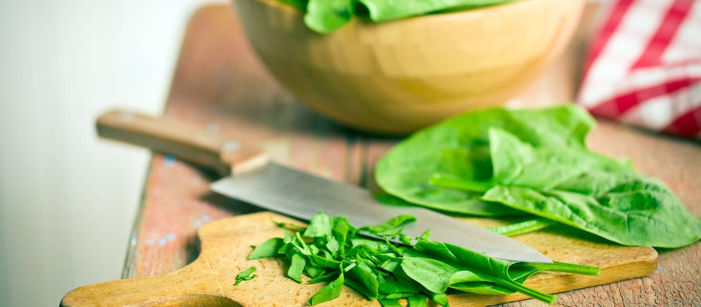 Spinat liegt geschnitten auf einem Brett. Spinat ist gesund und lecker. Mit welchen Rezepten schmeckt das Blattgemüse am besten? Und hilft Spinat möglicherweise beim Muskelaufbau? 