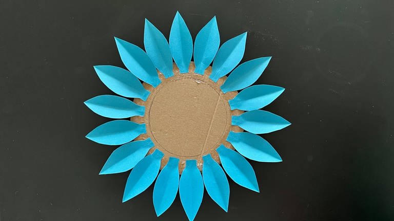 Aus festerem Papier Blüten ausschneiden und im Außenbereich das Kartonkreises  mit Bastelkleber festkleben. (Foto: Stefanie Renk)