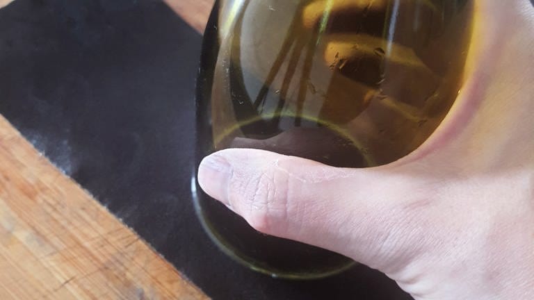 Das Schleifpapier auf den Arbeitstisch legen und mit der geschnittenen Seite der Weinflasche nun mit leichtem Druck darüber reiben, um die gerade Schnittseite abzuschleifen.
