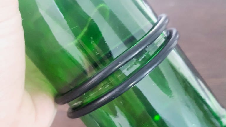 Anschließend zwei dem Glasschneideset beiliegende Gummiringe (richtige Größe zur Flasche auswählen) nehmen und diese an beiden Seiten der Schnittmarke  positionieren.