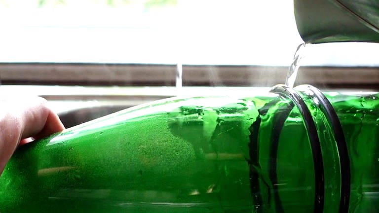 Weinflasche abwechselnd mit dem kochenden Wasser (aus dem Wasserkocher) und anschließend sofort mit dem kalten Wasser (aus dem Wasserhahn) zu übergießen.