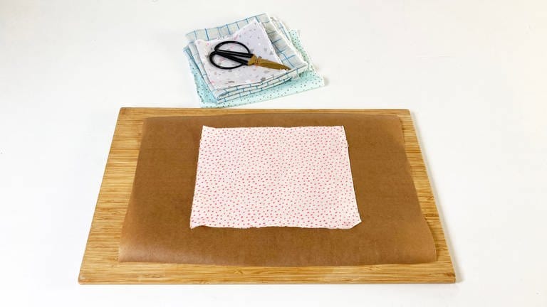 Auf einer Unterlage (z.b. einem Holzbrett) ein Stück Backpapier ausbreiten und den zugeschnittenen Baumwollstoff darauf platzieren.  (Foto: Iris Knabenschuh)