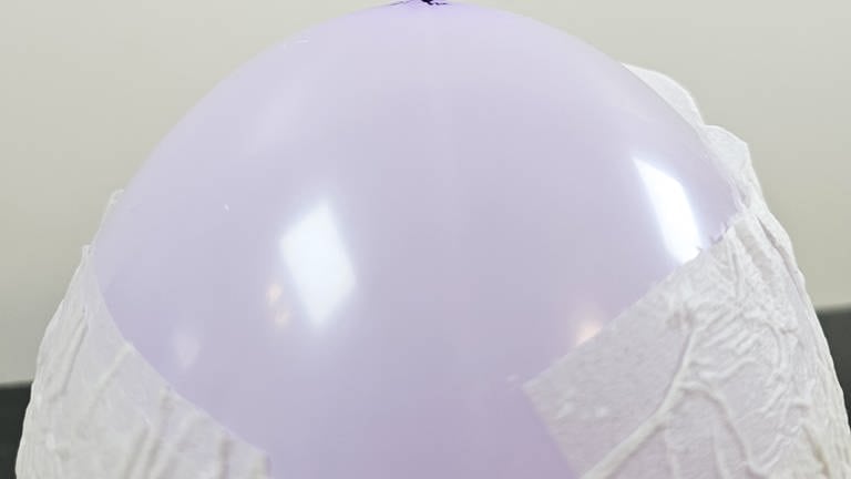 Wasser auf den Boden des Luftballons tropfen oder sprühen und ein Blatt Klopapier auf die feuchte Stelle legen. Nochmals Wasser auf das Papier geben bis alle Stellen möglichst flach und glatt am Luftballon anliegen. (Foto: Lisa Vöhringer)