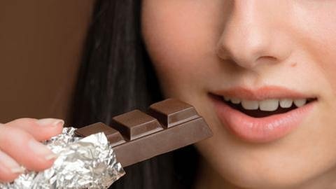 Frau hält einen Riegel Schokolade in ihrer Hand, und schaut mit geöffnetem Mund genussvoll darauf. (Foto: Getty Images, Thinkstock -)