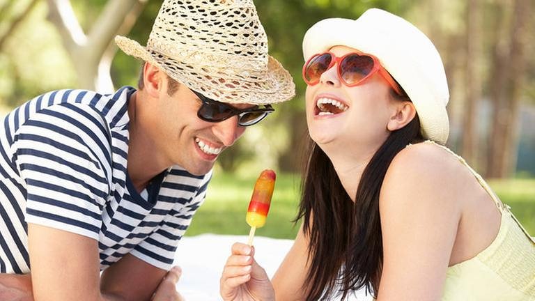 Junges Paar mit Sonnenhütten auf dem Kopf lacht und isst Eis (Foto: Getty Images, Thinkstock -)