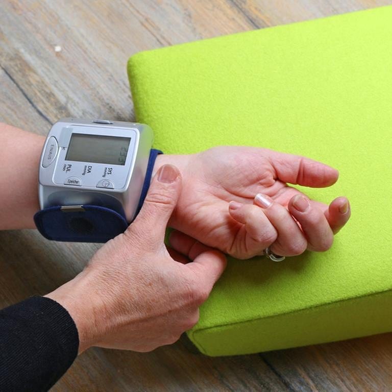 Arm liegt auf einem Kissen, mit einem Blutdruckmessgerät wird der Blutdruck am Handgelenk gemessen