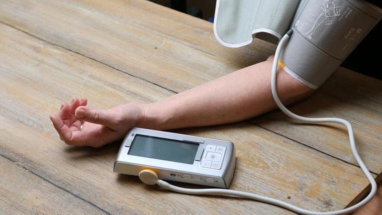 der Blutdruck wird am Oberarm mit einem Blutdruckmessgerät gemessen, der Arm liegt ruhig auf der Tischplatte (Foto: SWR, SWR -)