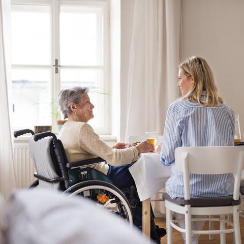Ältere Frau im Rollstuhl und eine jüngere Frau sitzen am Tisch