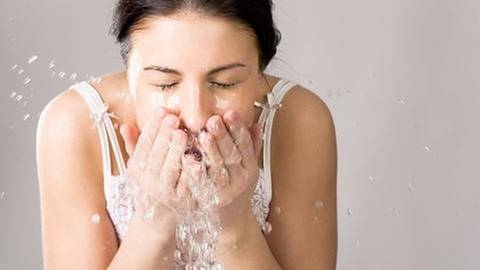 Eine Frau spritzt sich Wasser ins Gesicht.