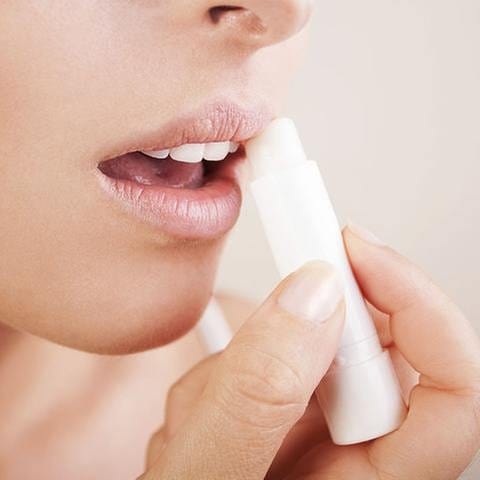 Eine Frau fettet sich die Lippen mit einem Pflegestift ein. (Foto: Getty Images, Thinkstock -)