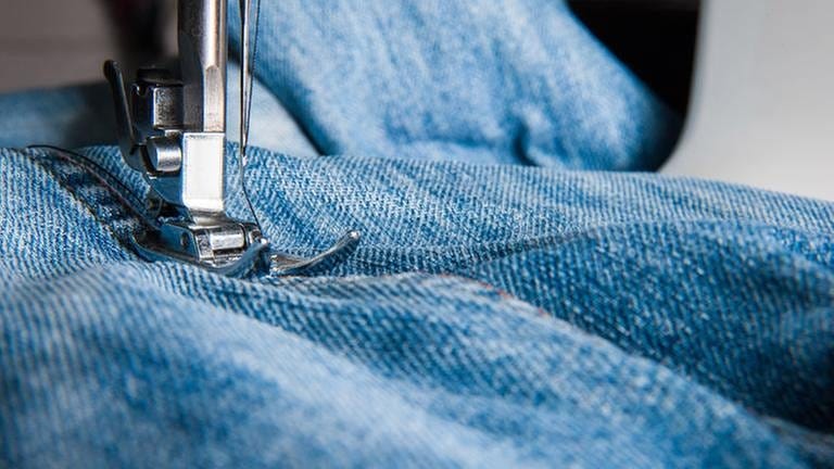 Eine Jeans wird mit Hilfe einer Nähmaschine repariert.
