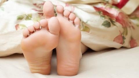 Füße schauen unter Decke auf einer Matratze hervor. (Foto: Getty Images, Thinkstock -)