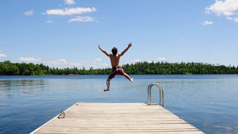 Junger Mann springt mit ausgestreckten Armen von einem Steg in einen Badesee. (Foto: Getty Images, Thinkstock -)