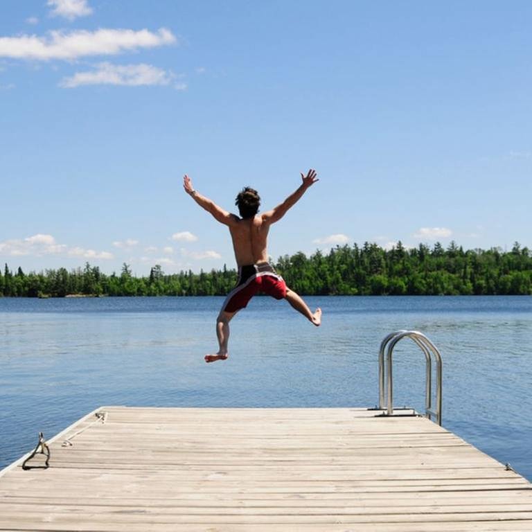 Junger Mann springt mit ausgestreckten Armen von einem Steg in einen Badesee. (Foto: Getty Images, Thinkstock -)