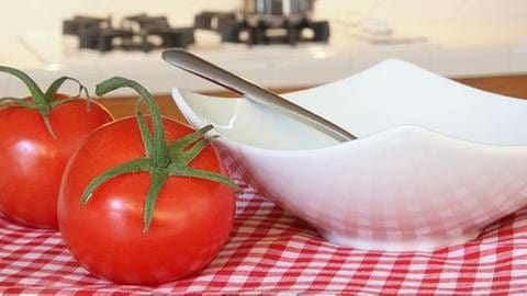 Eine Suppenschüssel mit Löffel steht neben reifen, frischen Tomaten in einer Küche.