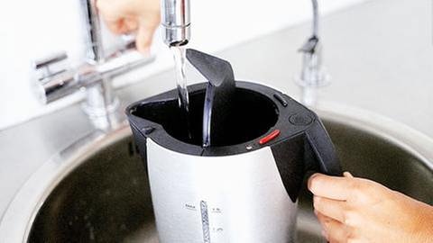 Frauenhände befüllen einen Wasserkocher unter dem Wasserhahn in der Küche. (Foto: Getty Images, Thinkstock -)